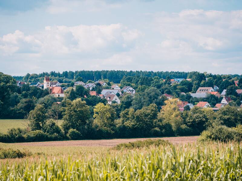Eine idyllische ländliche Szene zeigt Bussmannshausen mit einer Kirche, umgeben von Feldern und Bäumen unter einem bewölkten Himmel.