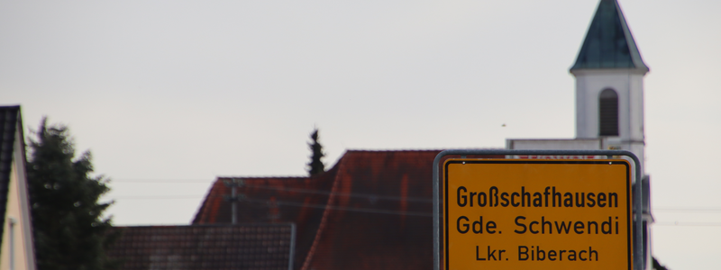 Bilde des Ortsschild von Großschafhausen von Orsenhausen kommend. Im Hintergrund ist die Kirche von Großschafhausen zu sehen.