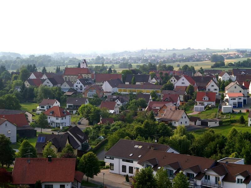 Bild von erhöhter Sicht aus der Ortsverwaltung Orsenhausen mit Blick in Richtung Kirche Orsenhausen. in der Mitte eine Straße die das Bild quer kreuzt. Links und rechts davon sind Bauernhäuser und relativ zentral auf der rechten Straßenseite ist die Kirch mit dem Kirchturm zu sehen.