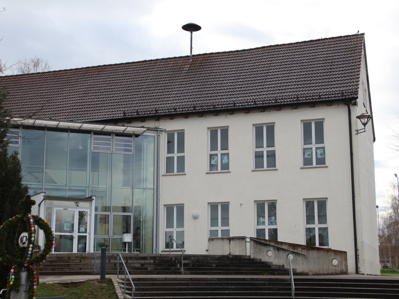 Bild der Grundschule und der Ortsverwaltung in Schönebürg. im Vordergrund ist ein gepflasterter Platz zu sehen,. Dahinter das Gebäude