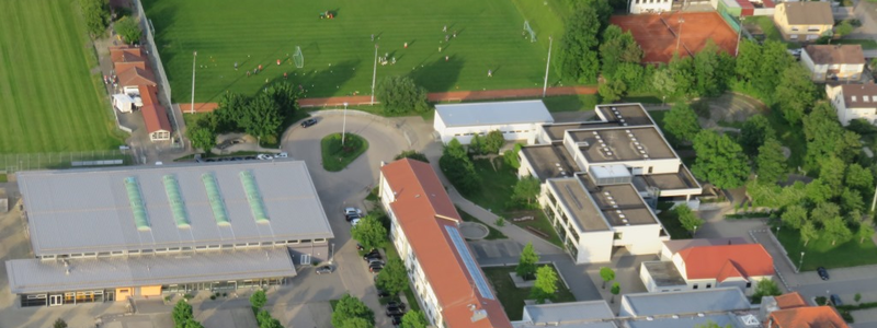 Luftbild vom Schulcampus in Schwendi, unten im Bild sind Wohnhäuser zu sehen, links im Bild ist die Sport- und Veranstaltungshalle, rechts die Max-Weishaupt Realschule und die Grund- und Werkrealschule, im Hintergrund ist der Sportplatz zu sehen