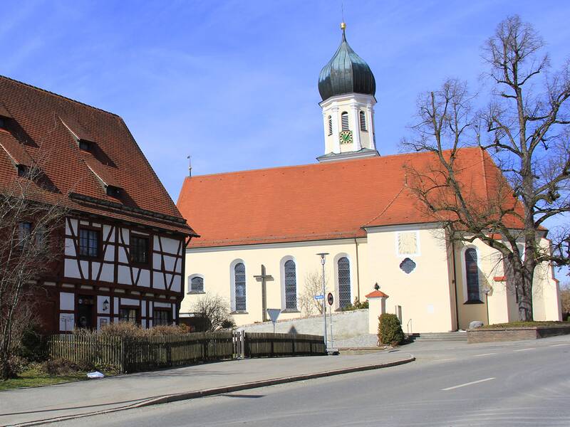 links im Bild ist ein altes Fachwerkhaus zu sehen. rechts davon ist eine Kirche zu sehen, deren Turm mittig über dem Gebäude ragt und einen Zwiebelturm hat. 