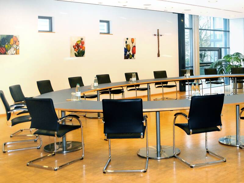 Bild des Sitzungssaal im Rathaus in Schwendi. Auf einem Holzboden steht ein ovaler Ring aus Tischen, die eine blaue Tischplatte haben. Um den Tisch herum stehen viele Stühle aus schwarzem Leder und silbernem Rahmen.