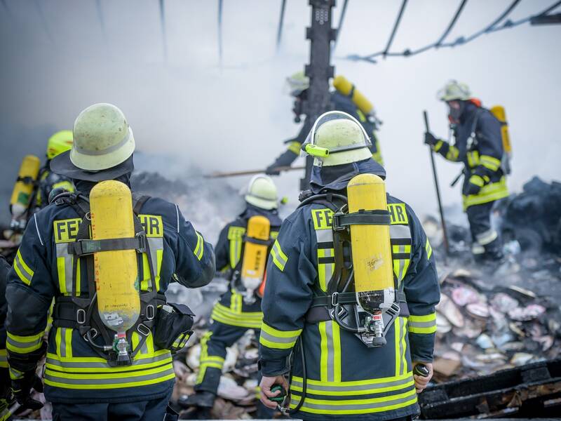 mehrere Feuerwehrmänner mit Atemschutzgeräten vor einem verbrannten Objekt